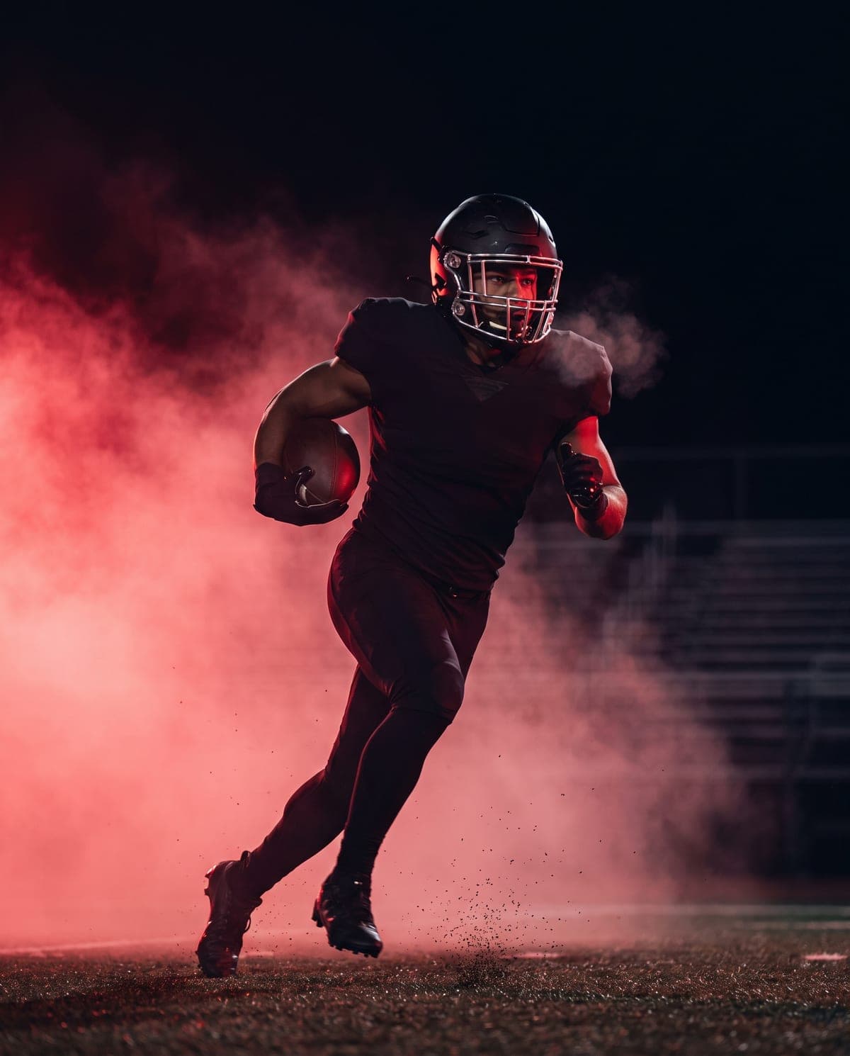 A ball carrier breaking through haze under floodlights at a night football game